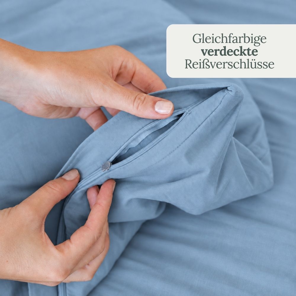 Hände öffnen den gleichfarbigen, verdeckten Reißverschluss der nebelblauen Perkal-Bettwäsche
