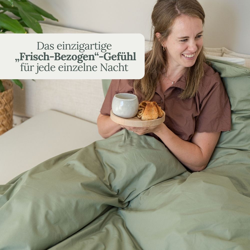 Lächelnde Frau mit Kaffee im Bett mit olivgrüner Perkal-Bettwäsche – frisch-bezogen-Gefühl