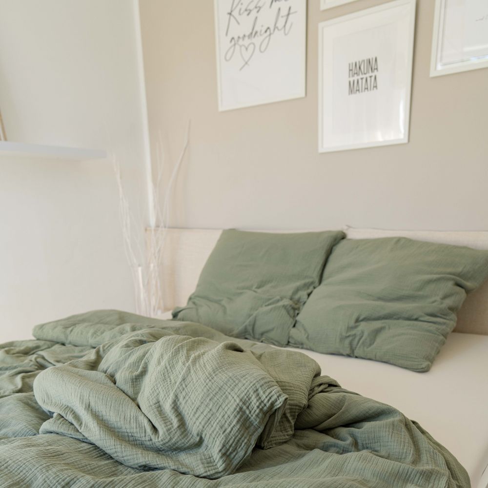 Schlafzimmer mit Bett in olivgrüner Musselin-Bettwäsche und Bildern an der Wand
