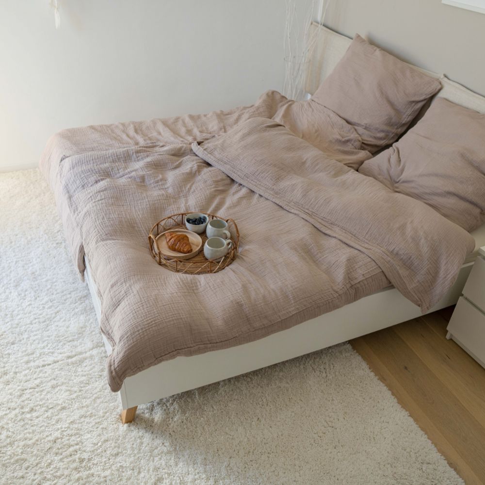 Bett mit taupefarbener Musselin-Bettwäsche und Frühstückstablett auf hellem Teppich
