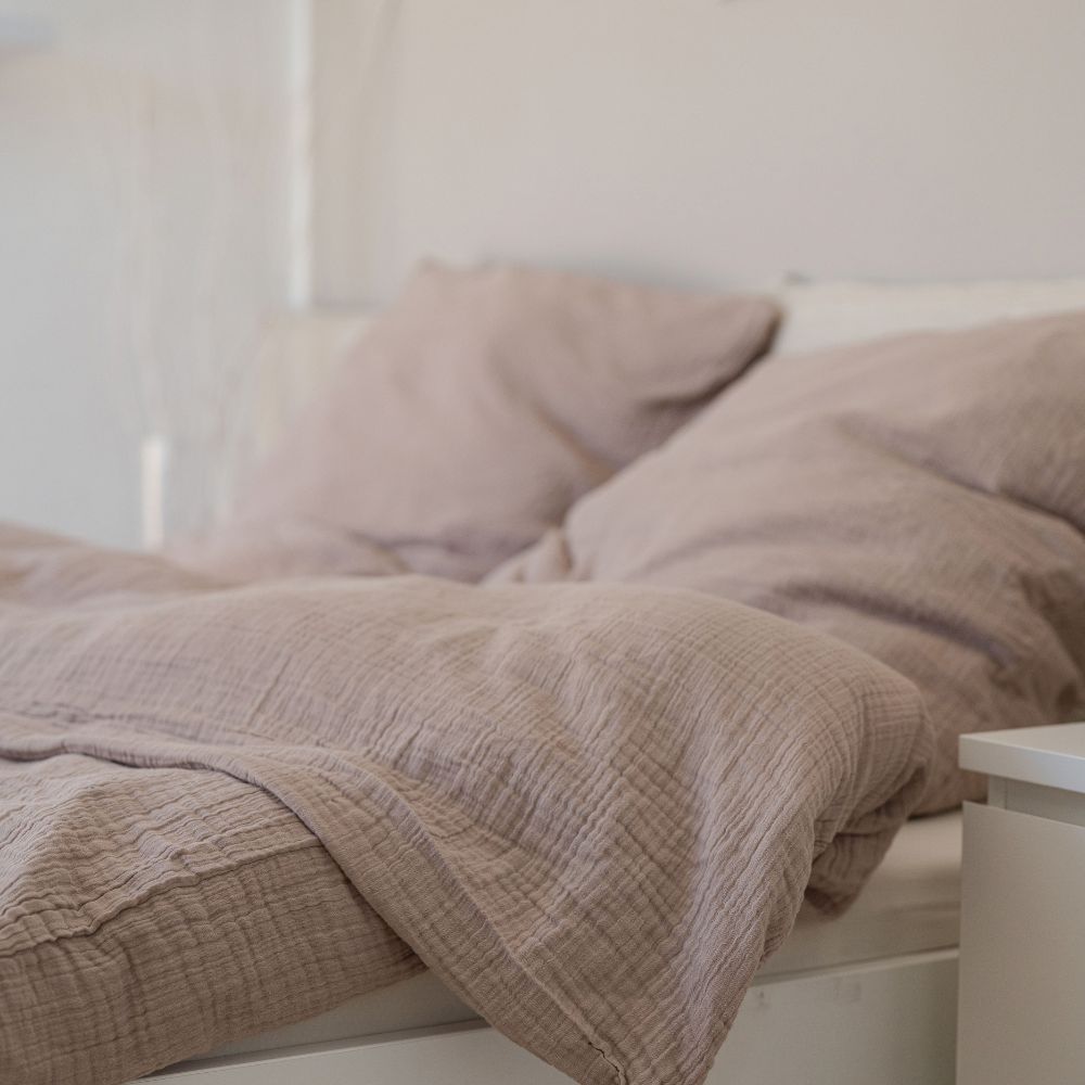 Taupefarbene Musselin-Bettwäsche aus Bio-Baumwolle mit Kopfkissen auf einem hellen Bett
