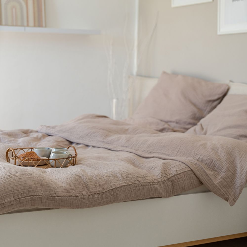 Bett mit taupefarbener Musselin-Bettwäsche und Frühstückstablett im hellen Schlafzimmer