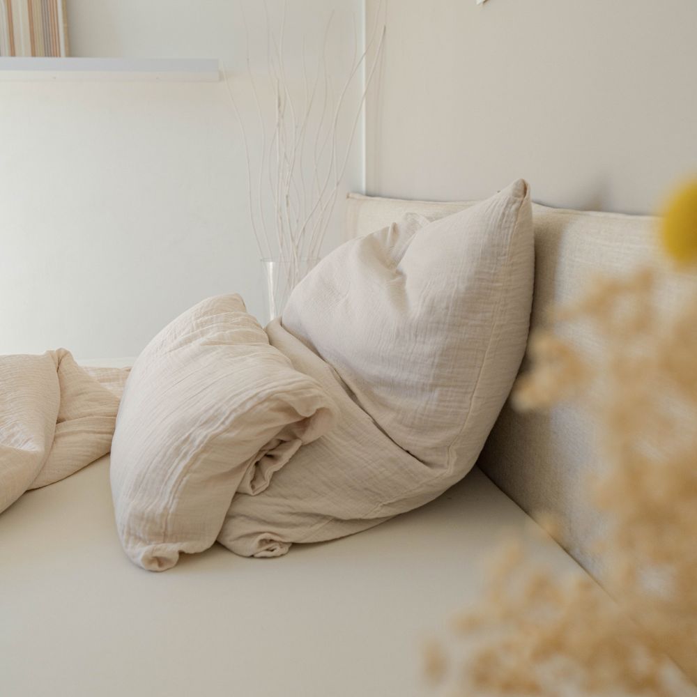 Cremefarbene Musselin-Kopfkissen auf einem hellen Bett mit Trockenblumen im Vordergrund