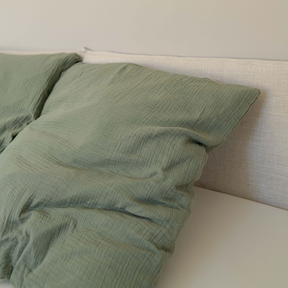 Zwei olivgrüne Musselin-Kopfkissen aus Bio-Baumwolle auf einem hellen Bett