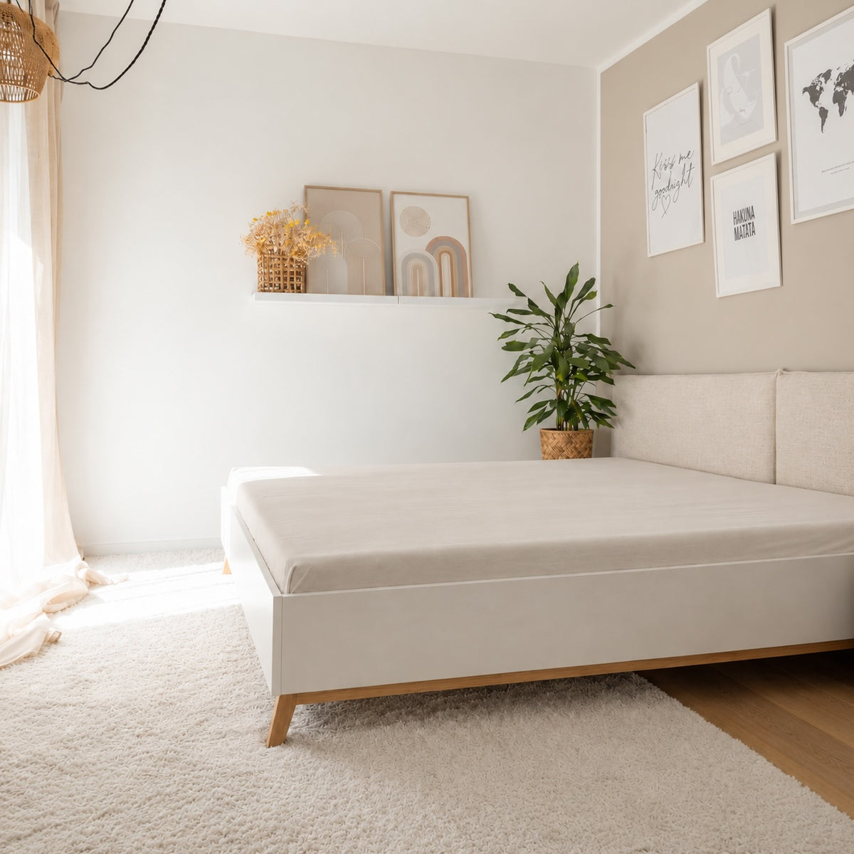Bett mit sandfarbenem Spannbettlaken in einem hellen Schlafzimmer mit Pflanze