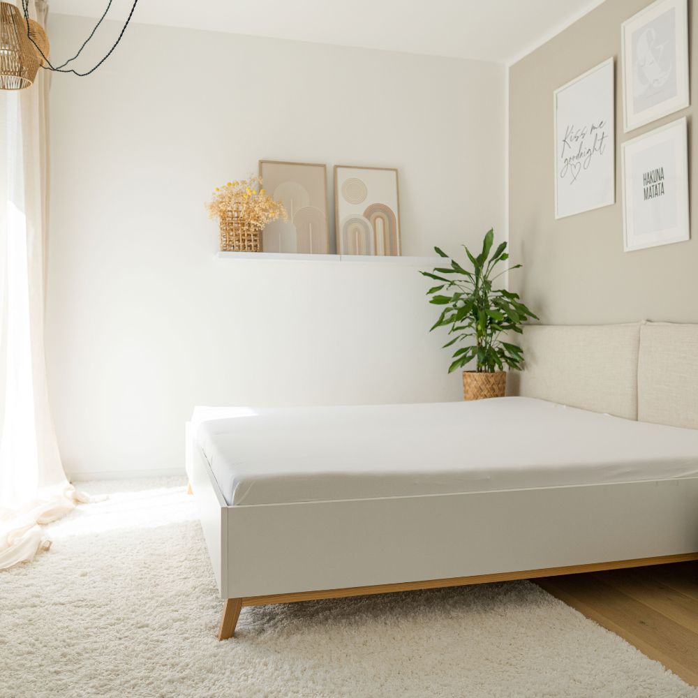Bett mit weißem Spannbettlaken in einem hellen Schlafzimmer mit Pflanze