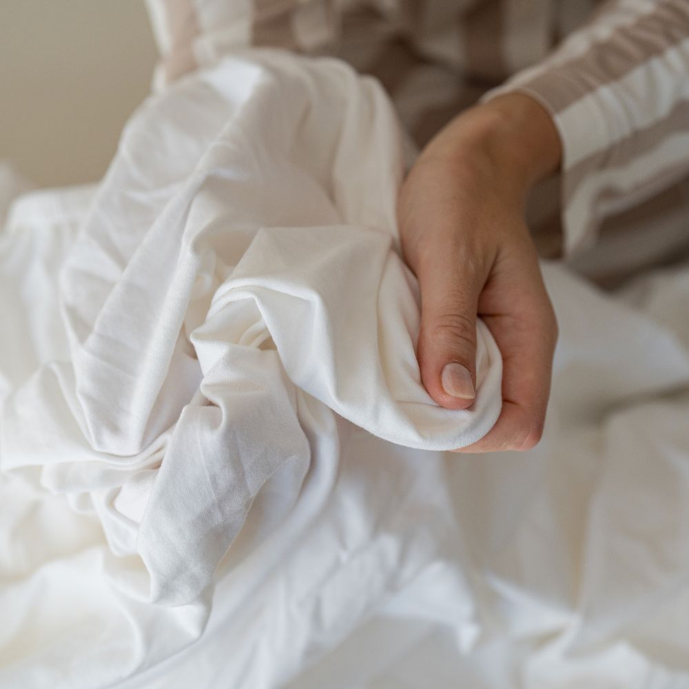 Hand greift in den weichen Stoff eines weißen Spannbettlakens aus Bio-Baumwolle