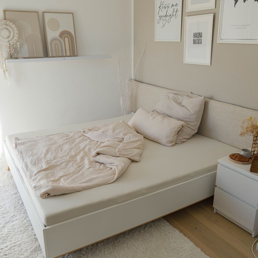 Helles Schlafzimmer mit Bett in cremefarbener Musselin-Bettwäsche und Bildern an der Wand