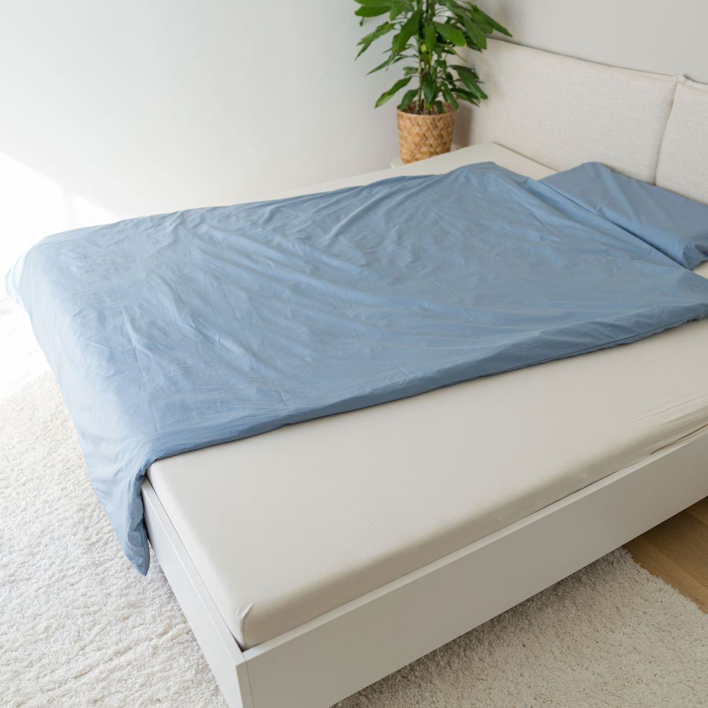 Bett mit nebelblauem Perkal-Deckenbezug aus Bio-Baumwolle im hellen Schlafzimmer