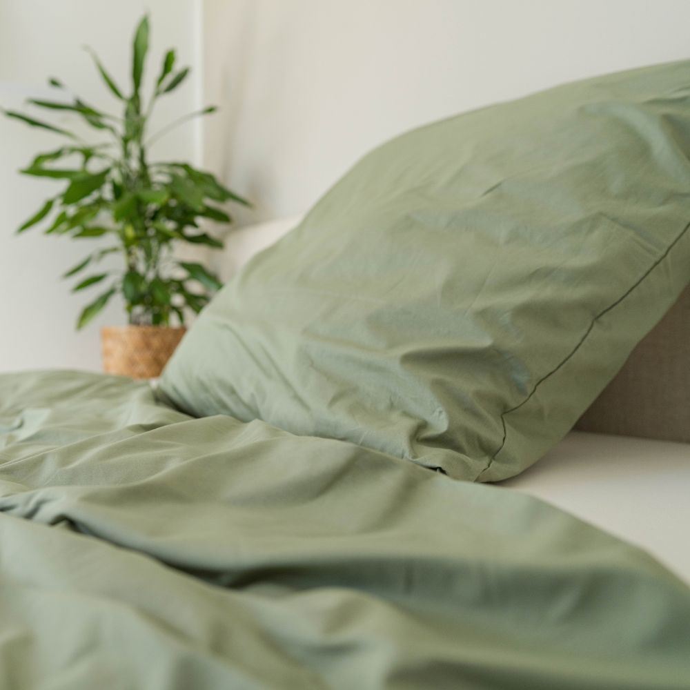 Olivgrüner Perkal-Kopfkissenbezug aus Bio-Baumwolle auf einem Bett mit Pflanze